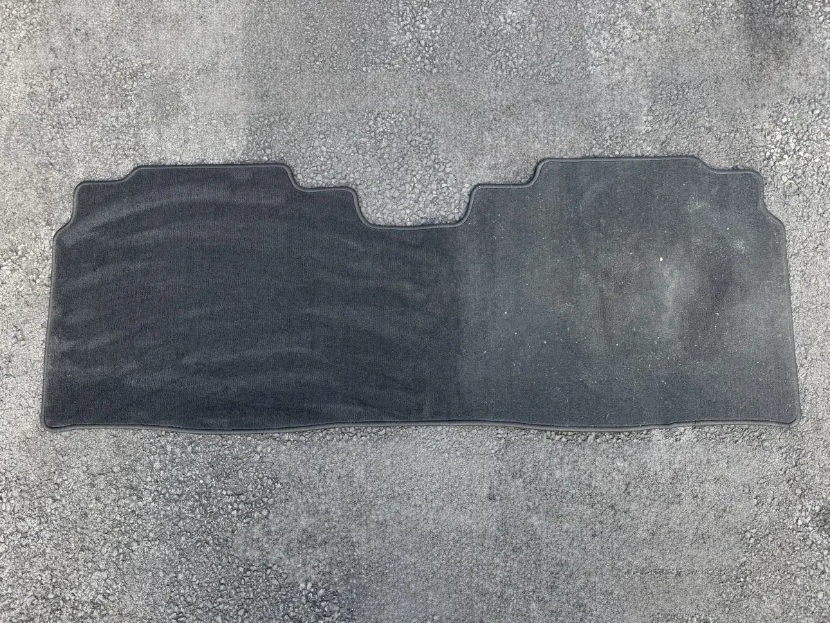 Gray carpet floor mat on a driveway, left half cleaned, right half still dirty