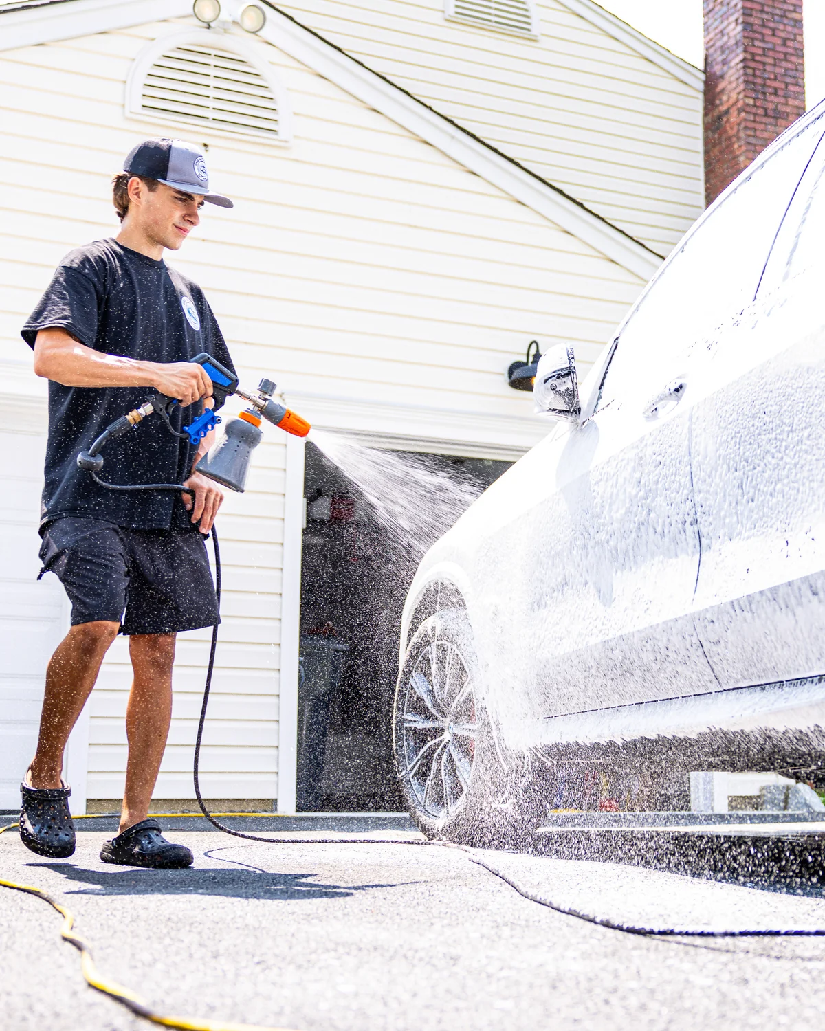 Christian foam cannon washing a white car in a Morris County driveway