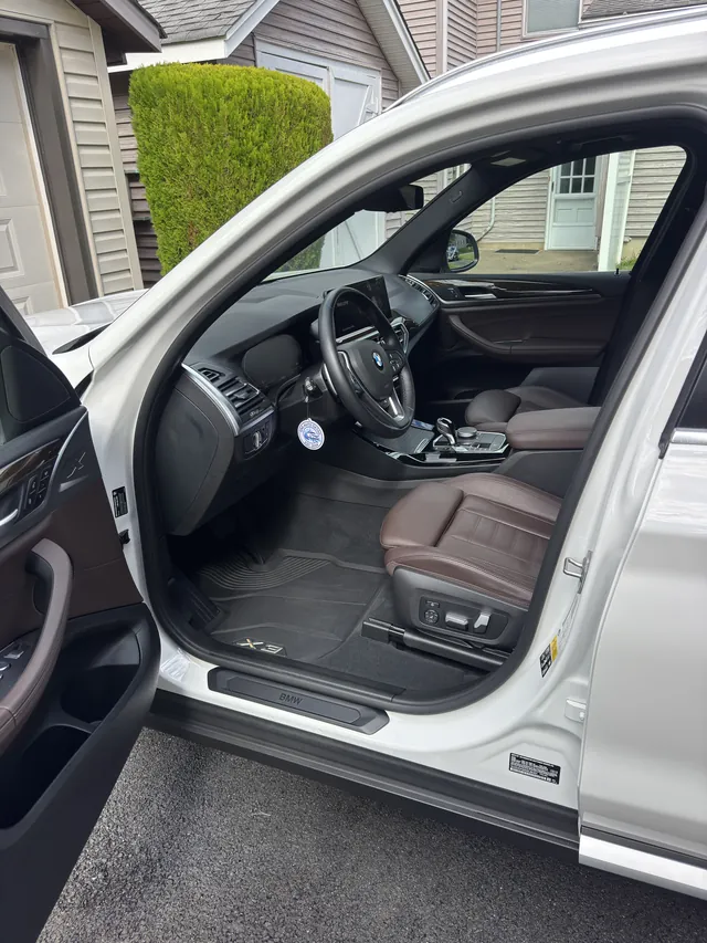 White BMW X3 with the door open showing clean mocha leather seats and floor mats after an interior detail