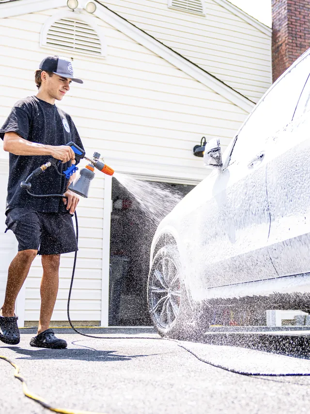 Christian spraying a thick foam pre-wash on a white SUV before the hand wash