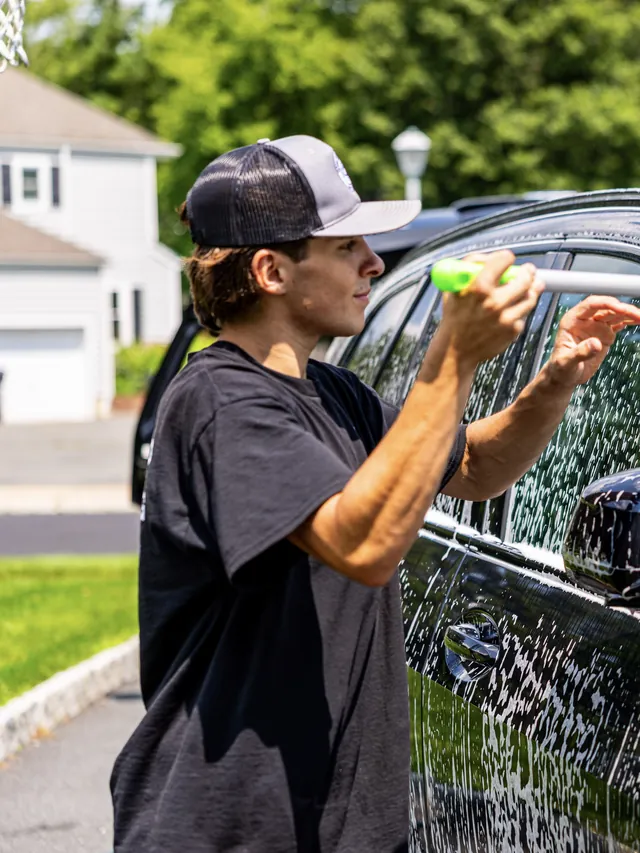 Christian hand washing a dark BMW SUV with a soapy wash mitt on a pole